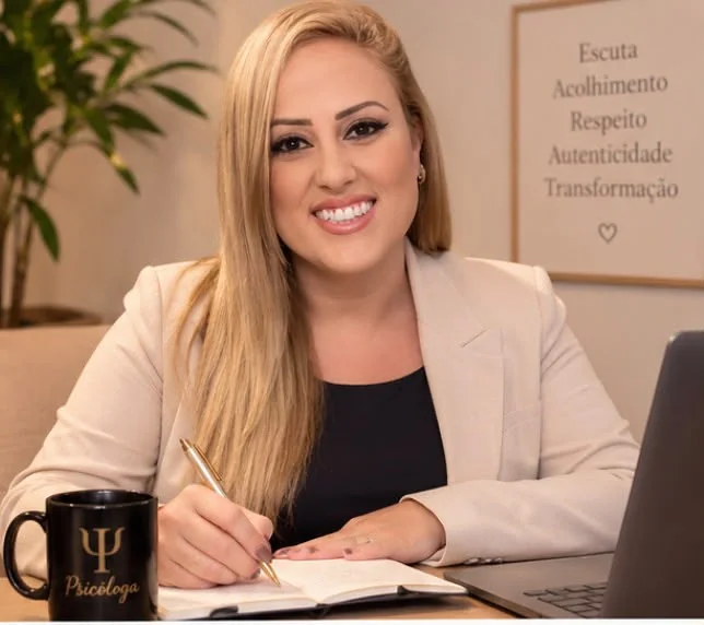 Fernanda Nunes Gonçalves, psicóloga clínica, à mesa de trabalho, escrevendo em um caderno ao lado do notebook